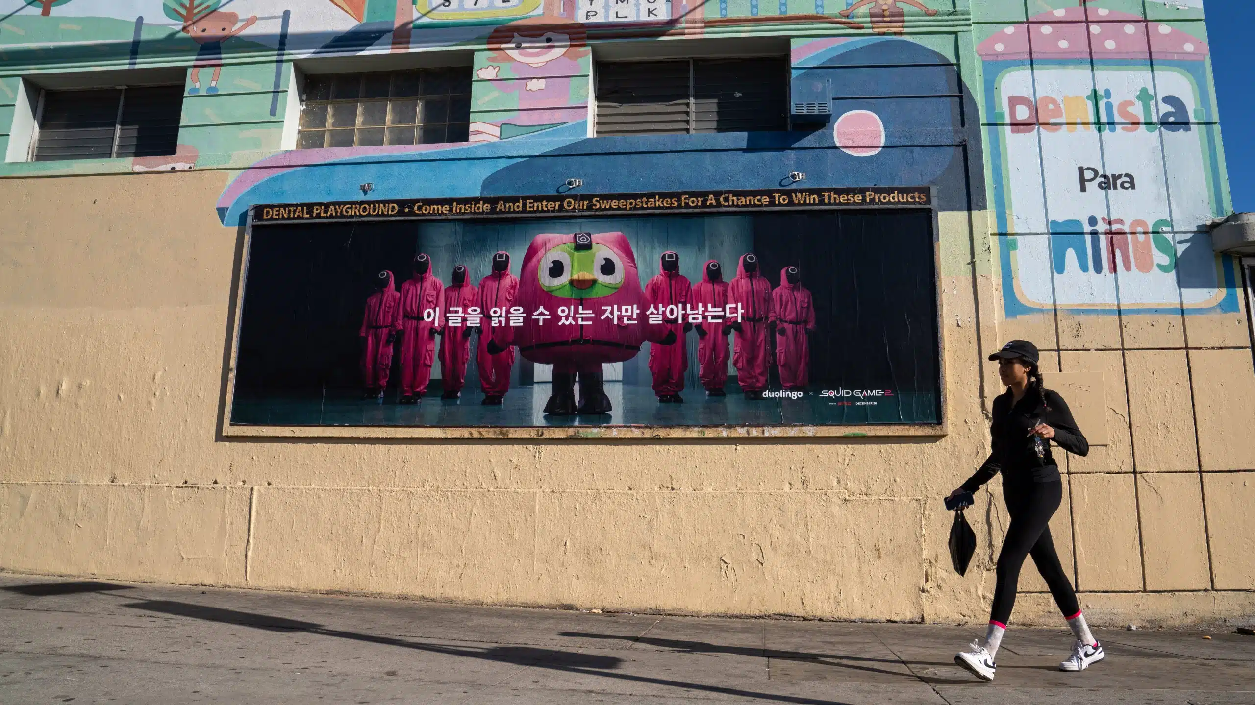 Eye-Catching Squid Game and Duolingo Street Advertisement at 3631 W 3rd St, Los Angeles 🌟 WILD POSTING® Street mural in Los Angeles depicting Duolingo's owl mascot surrounded by Squid Game characters in pink suits.