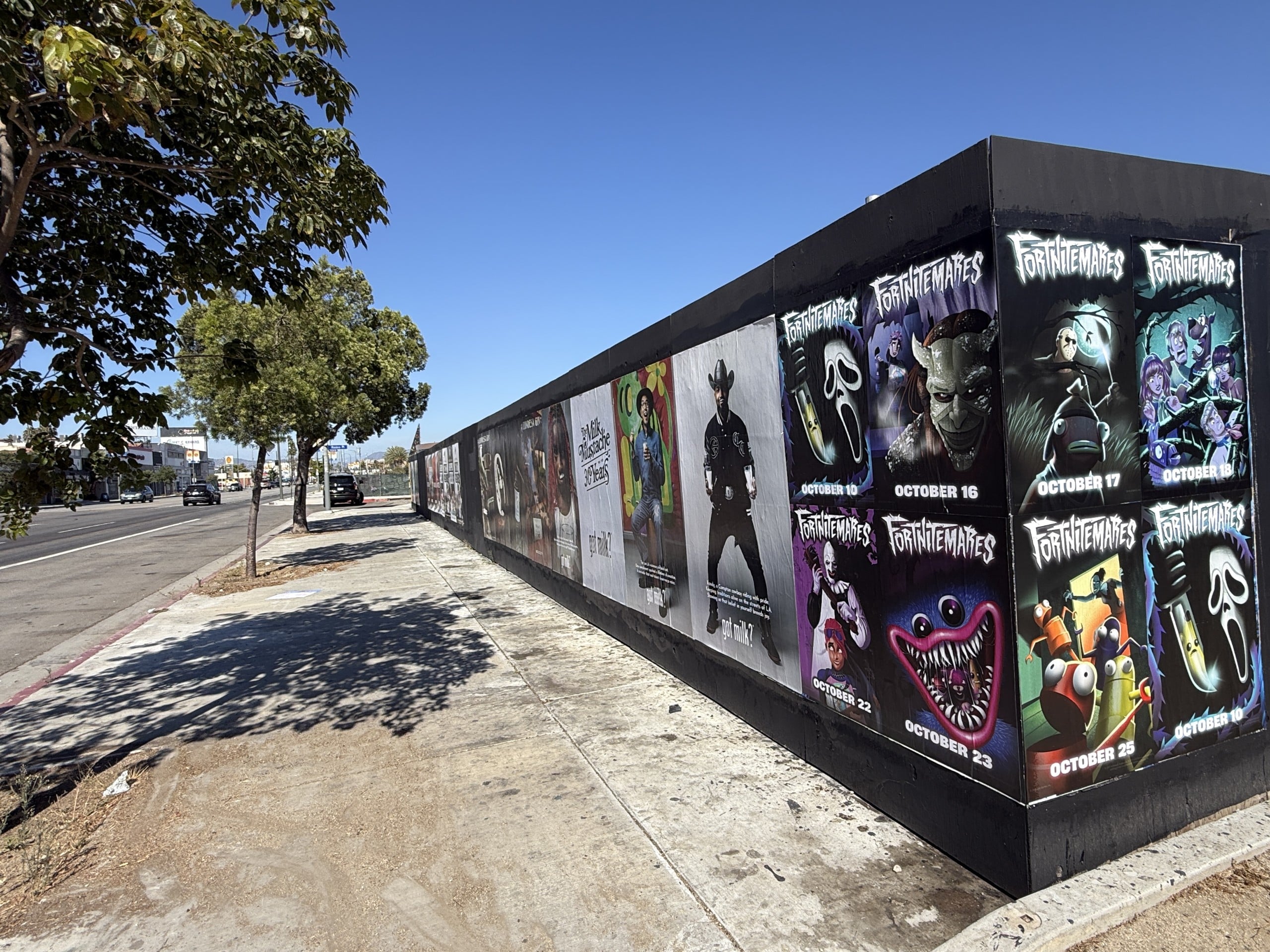 Wild Posting® posters for FortniteMares and LA Rams along a construction wall on S Hope St in Downtown Los Angeles, with pedestrians and surrounding street context.