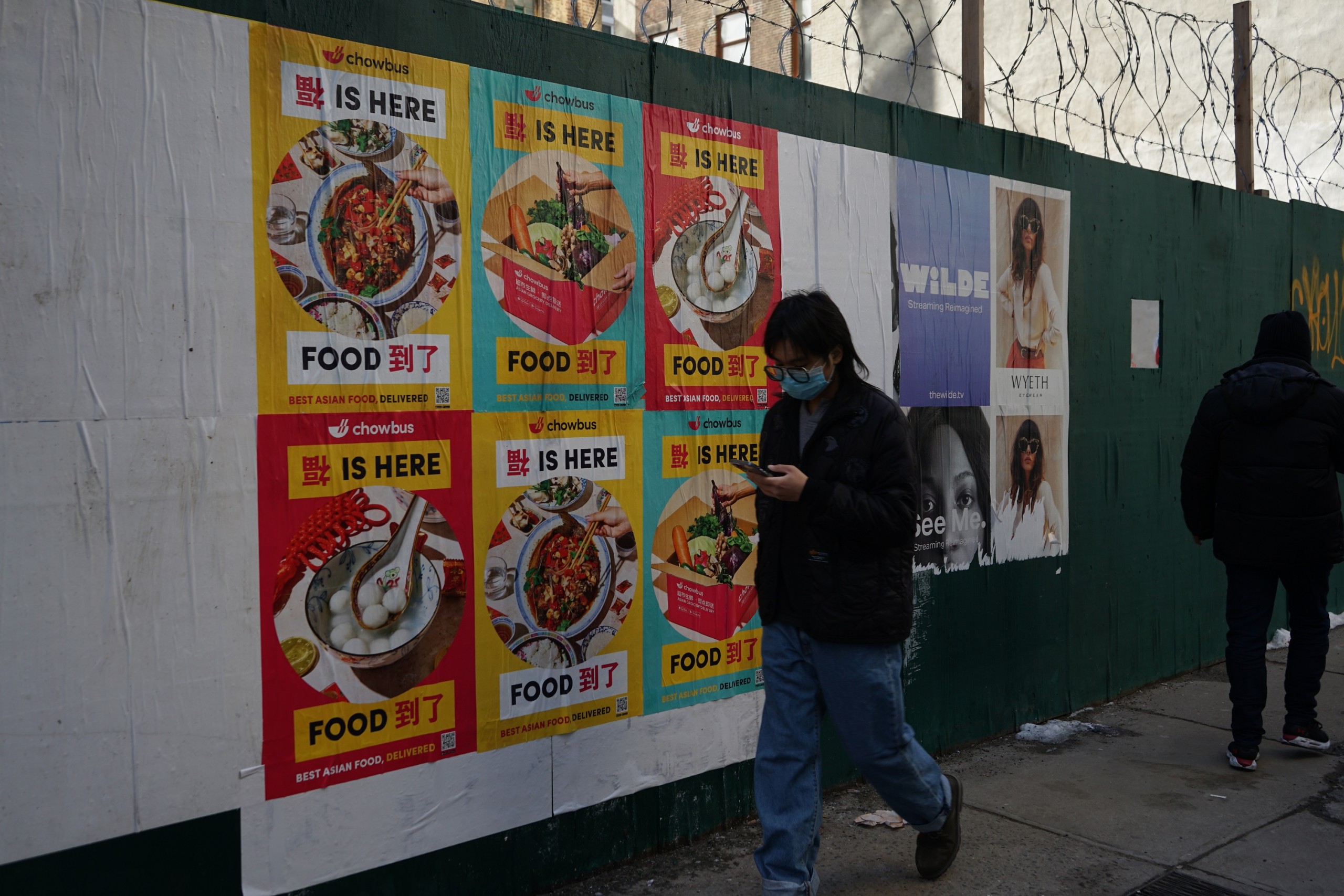 Chowbus Wild Posting® posters displayed on a New York City construction wall along a busy sidewalk