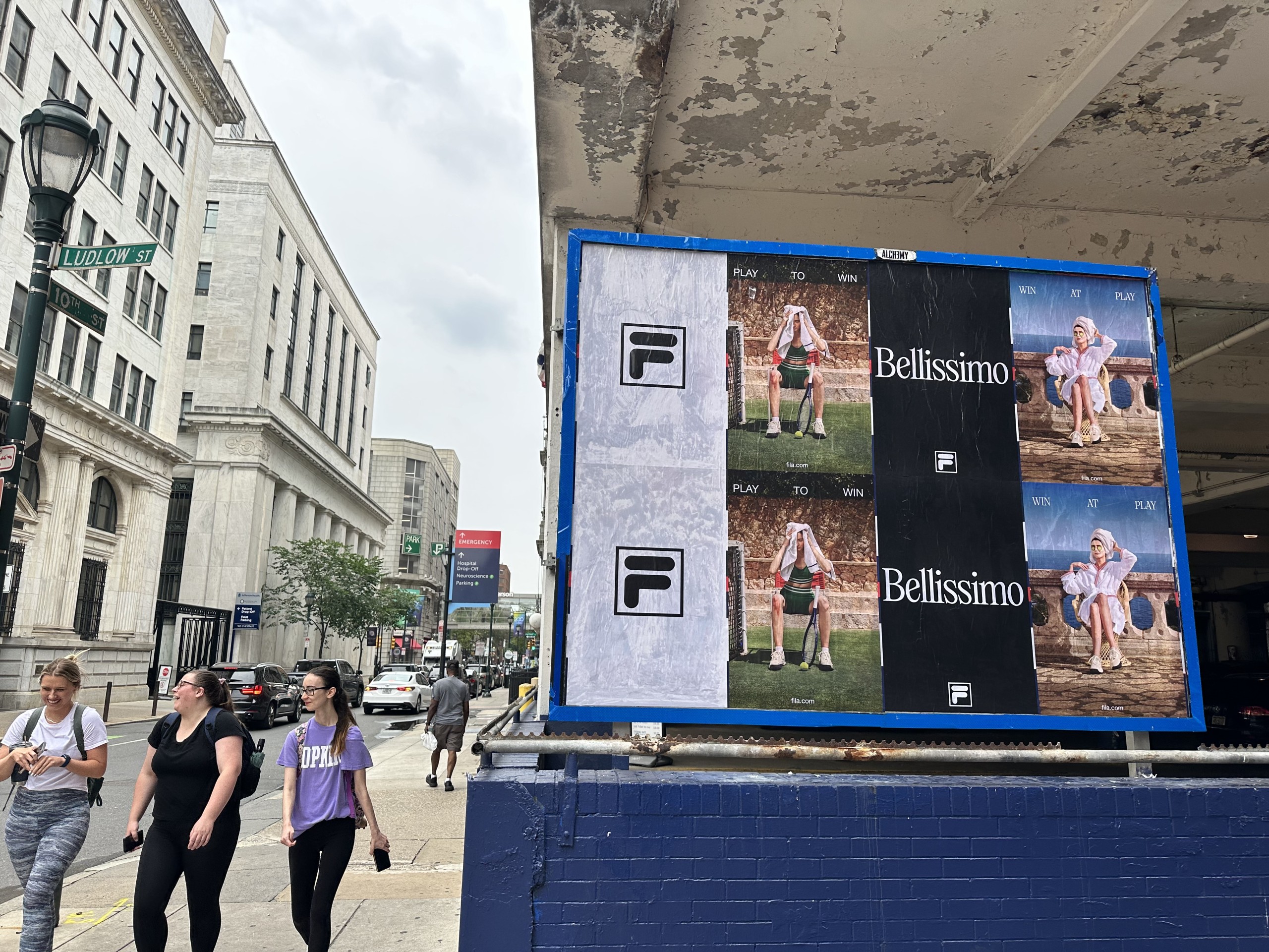 Fila Bellissimo Wild Posting® posters installed on a street-level construction wrap along a busy downtown sidewalk