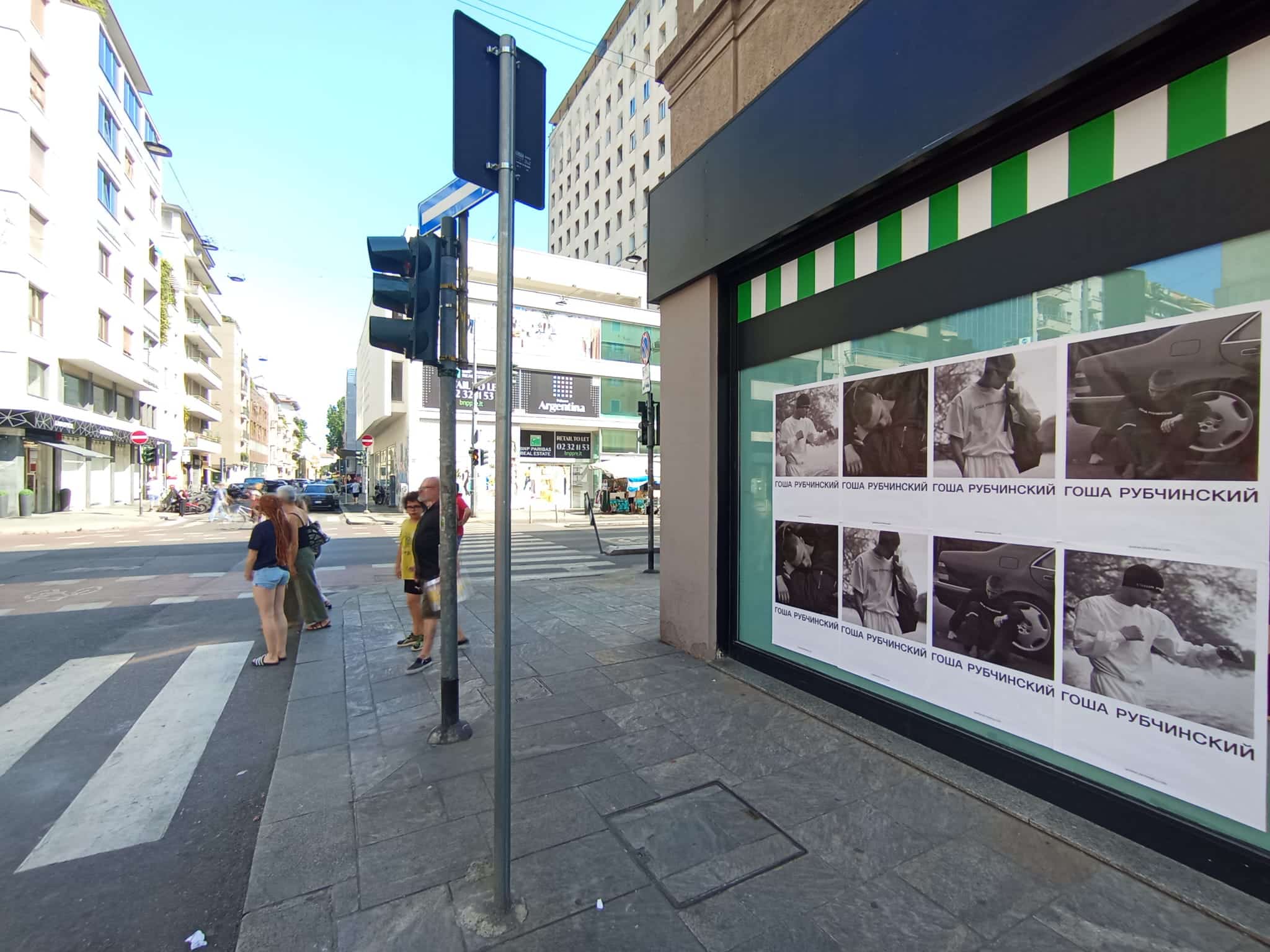Gosha Rubchinskiy Wild Posting® campaign displayed in a storefront window along a busy European city street, featuring black-and-white fashion poster layouts.