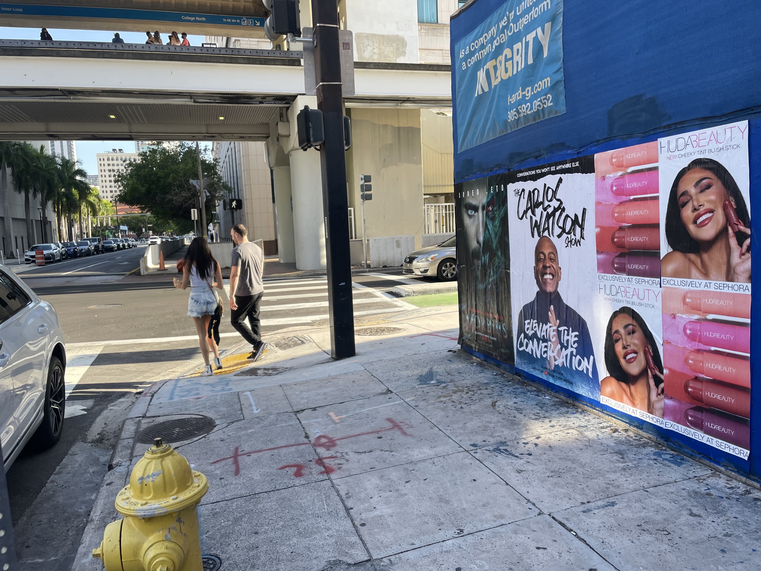 Huda Beauty Wild Posting® campaign installed at a high-traffic intersection beneath elevated transit in downtown Miami