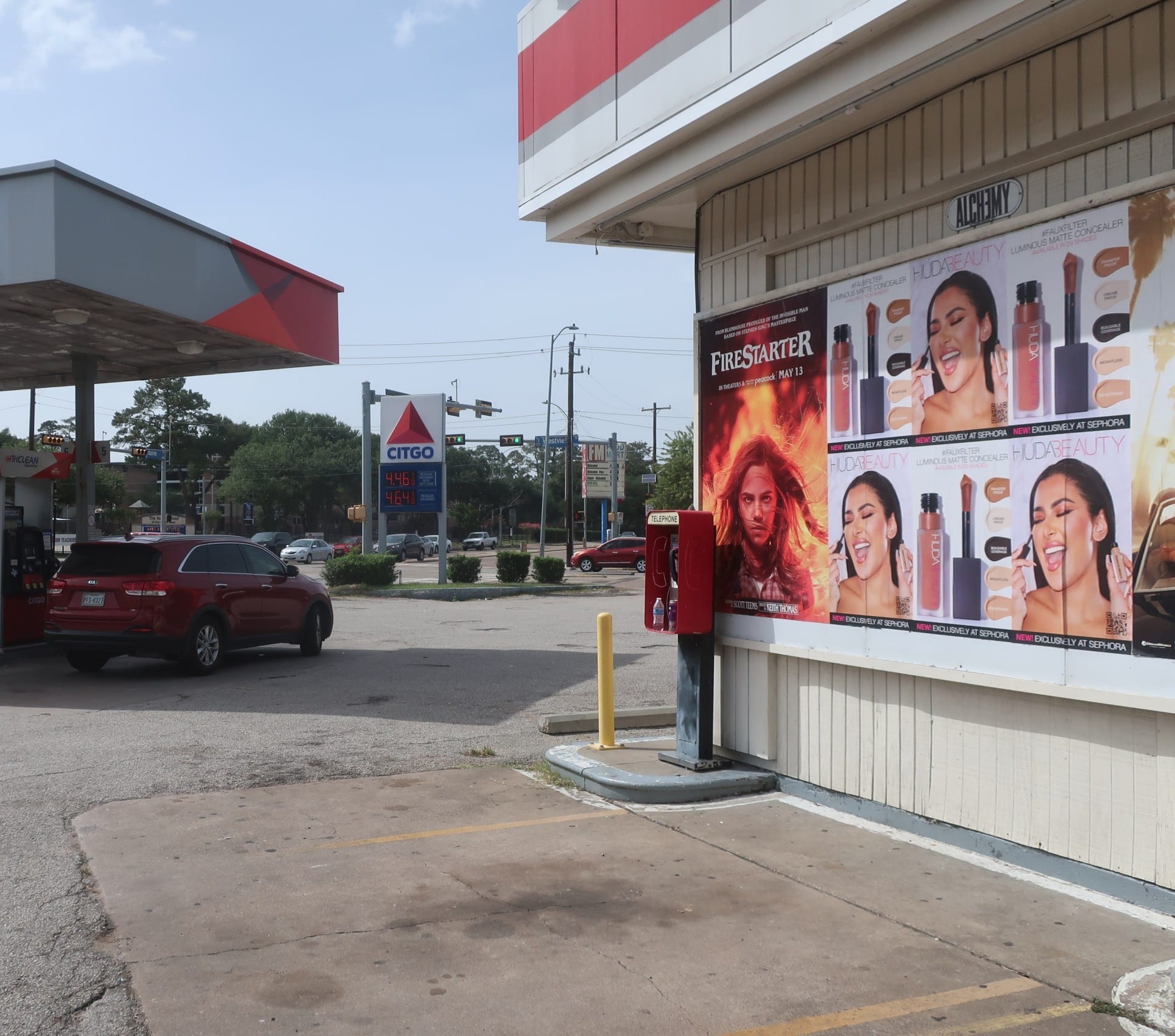 Huda Beauty Wild Posting® posters displayed at a busy gas station corner with passing vehicle traffic