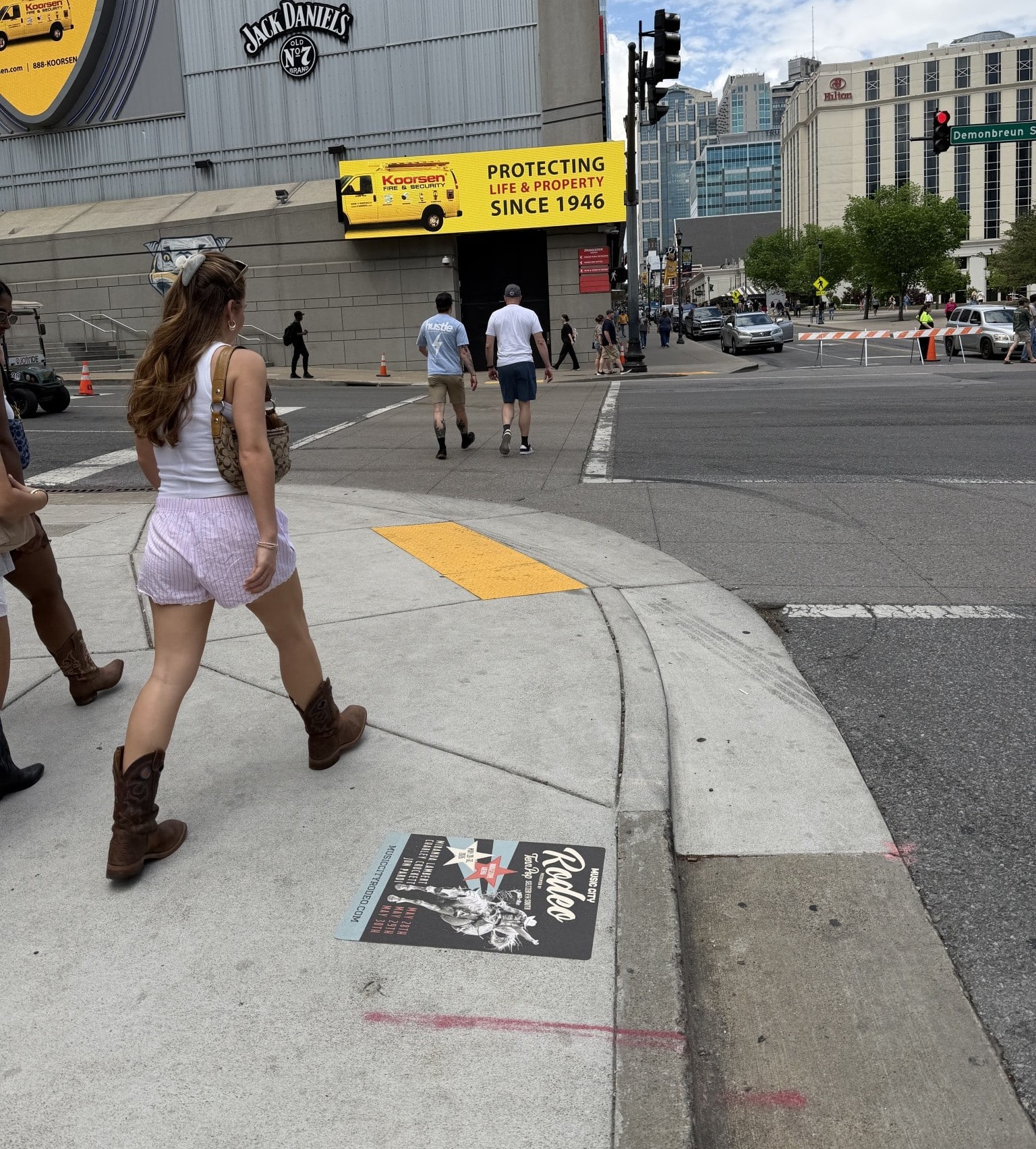 Sidewalk decal advertising a Music City Rodeo event installed outside Bridgestone Arena in downtown Nashville, with a pedestrian in cowboy boots walking past.