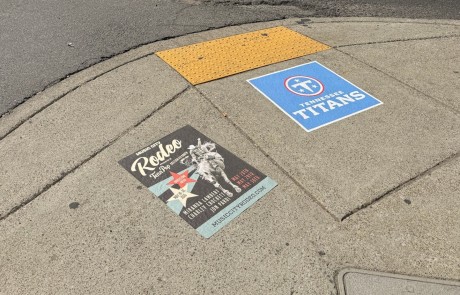 Two sidewalk decals installed on a Nashville crosswalk corner — a Tennessee Titans NFL decal and a Music City Rodeo event decal — at the intersection of Broadway in downtown Nashville.