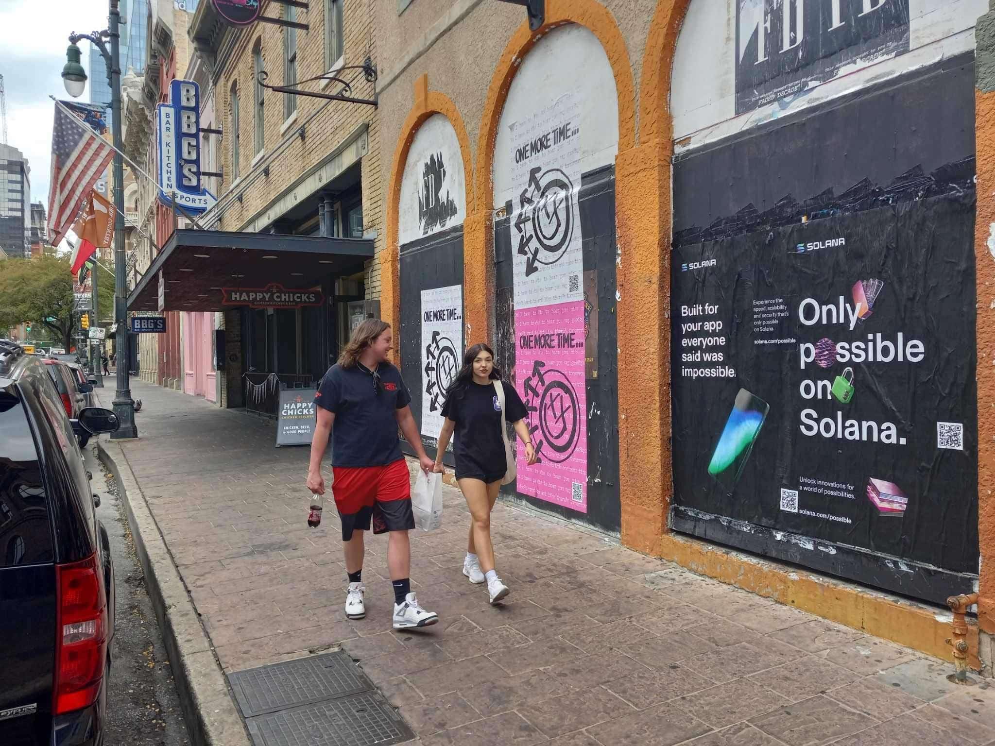 Wild Posting® posters for Solana and Blink-182 displayed on boarded storefront arches at 6th St & Brazos in Austin, with pedestrians walking past.