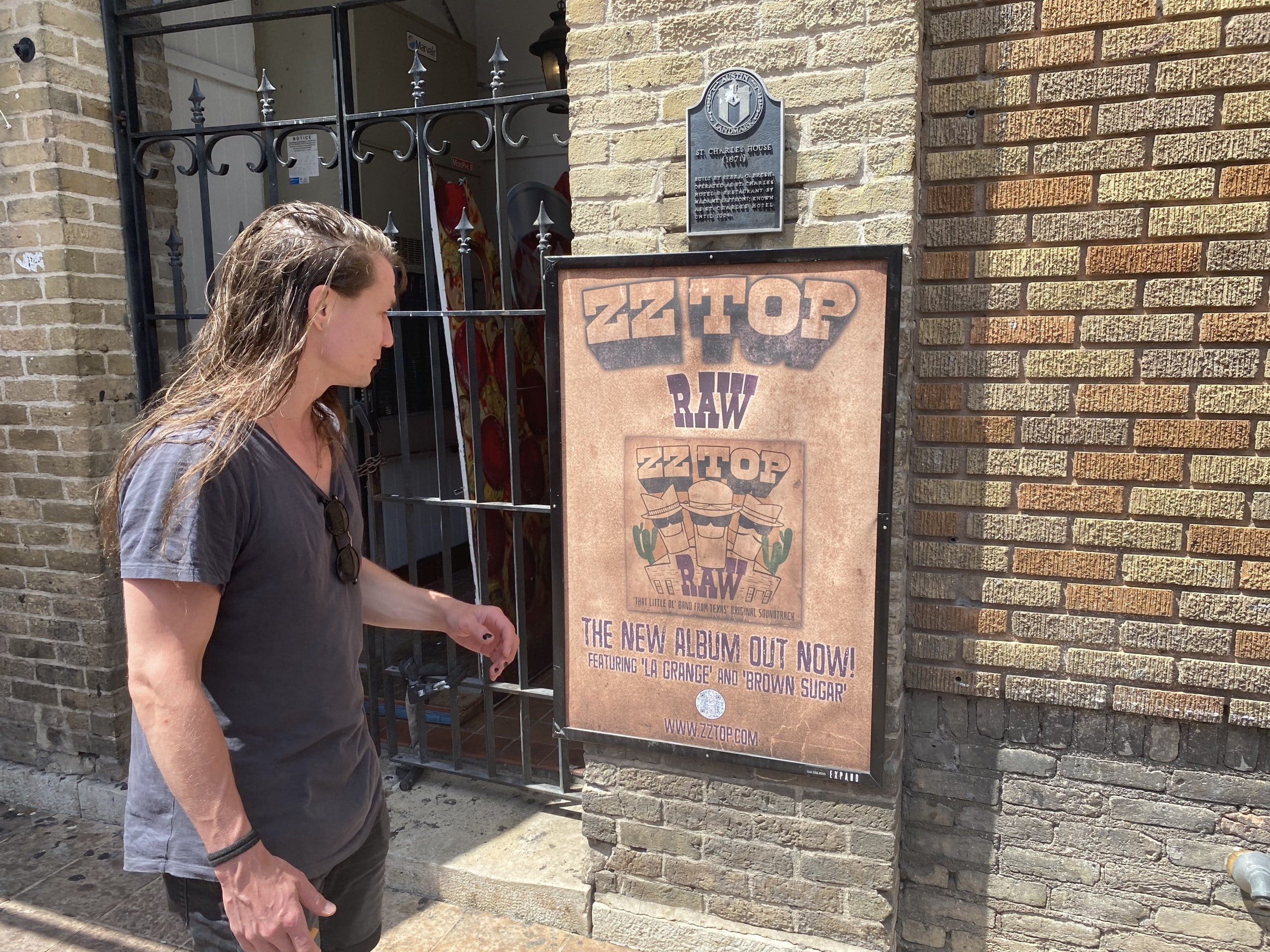 Wild Posting® poster for ZZ Top’s “RAW” album mounted on a brick wall in Austin, Texas, with a pedestrian viewing the display.