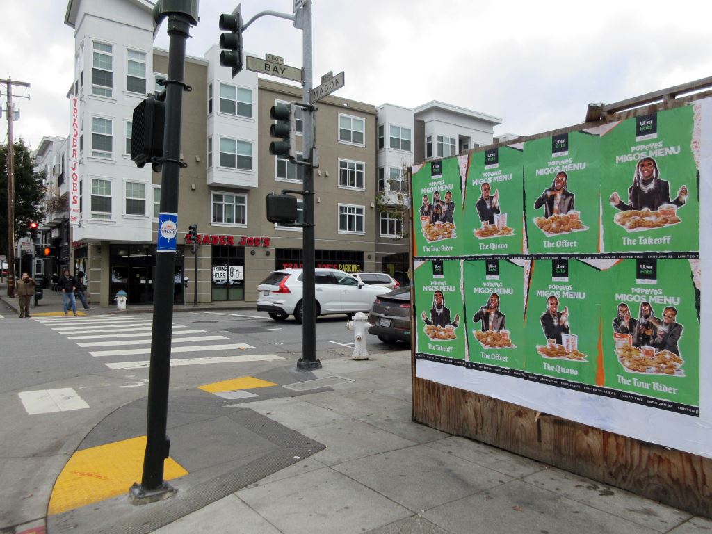Wild Posting® posters for Uber Eats Migos Menu on a street-level construction wall at Bay St & Mason St in San Francisco, near a busy intersection.