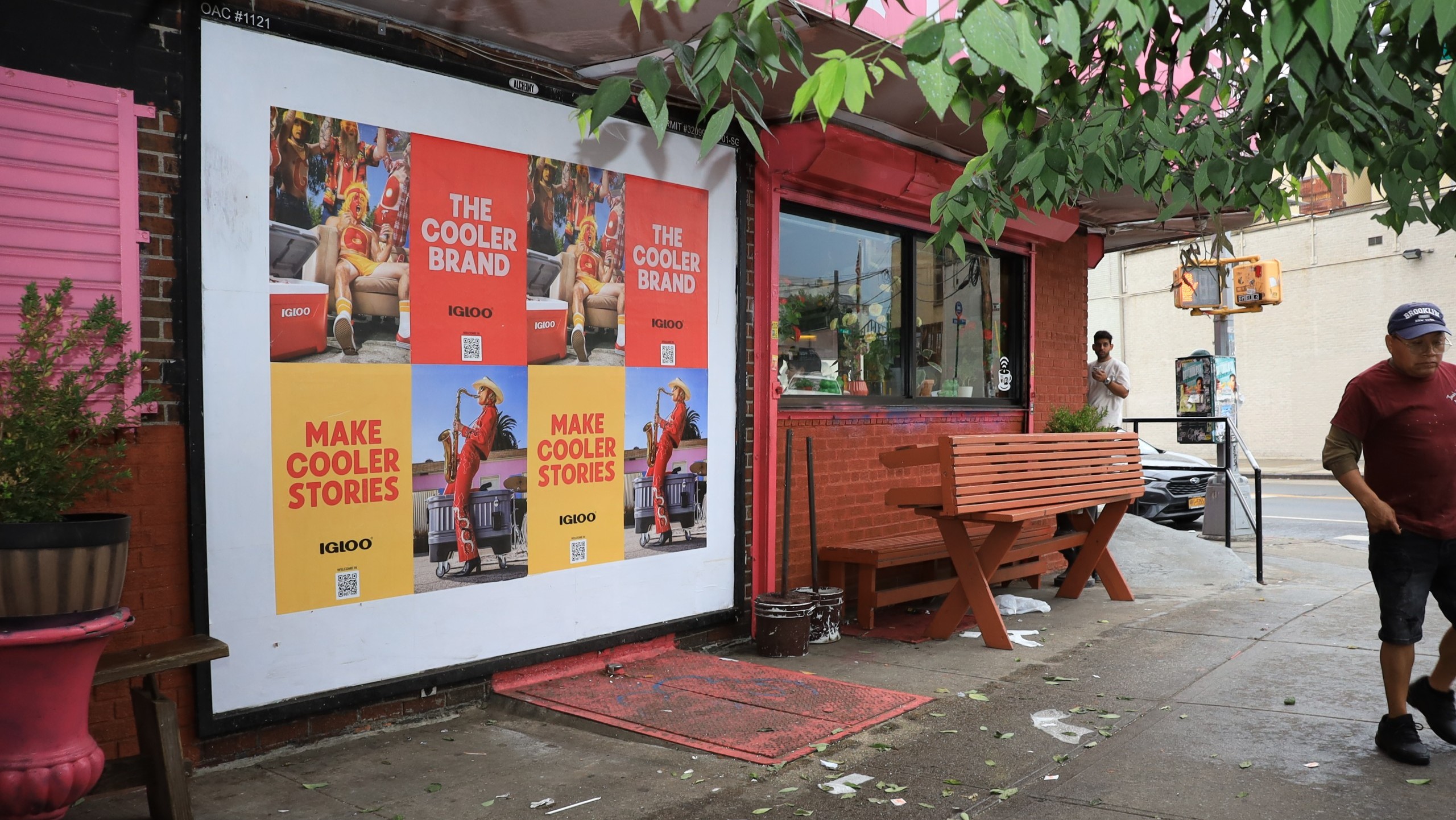 Igloo “Make Cooler Stories” Wild Posting® posters displayed on a storefront in Brooklyn, with a pedestrian walking by and colorful exterior details around the shop.