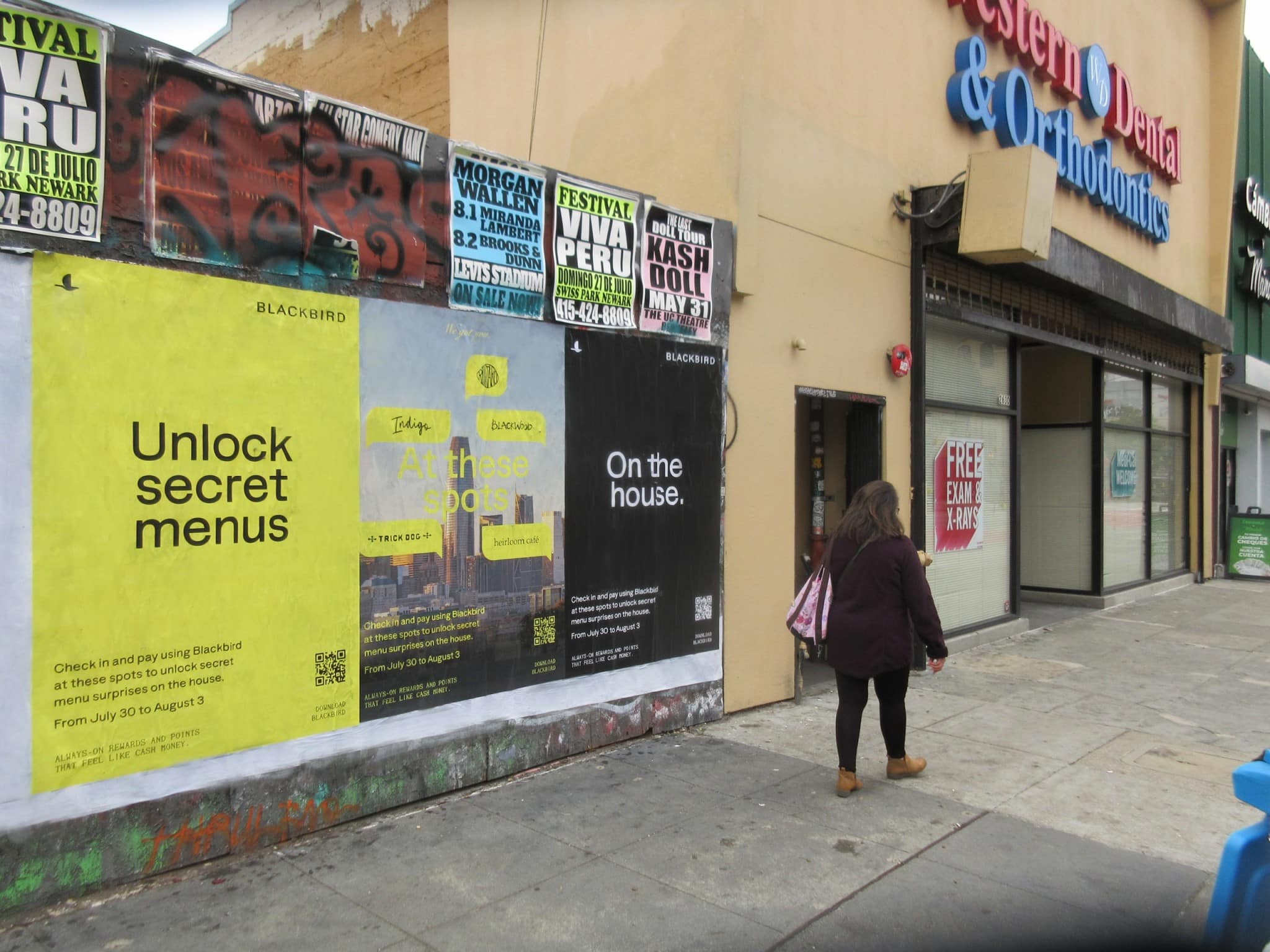Wild Posting® posters for Blackbird and live music events on a storefront wall at Mission St in San Francisco, with a pedestrian walking past.
