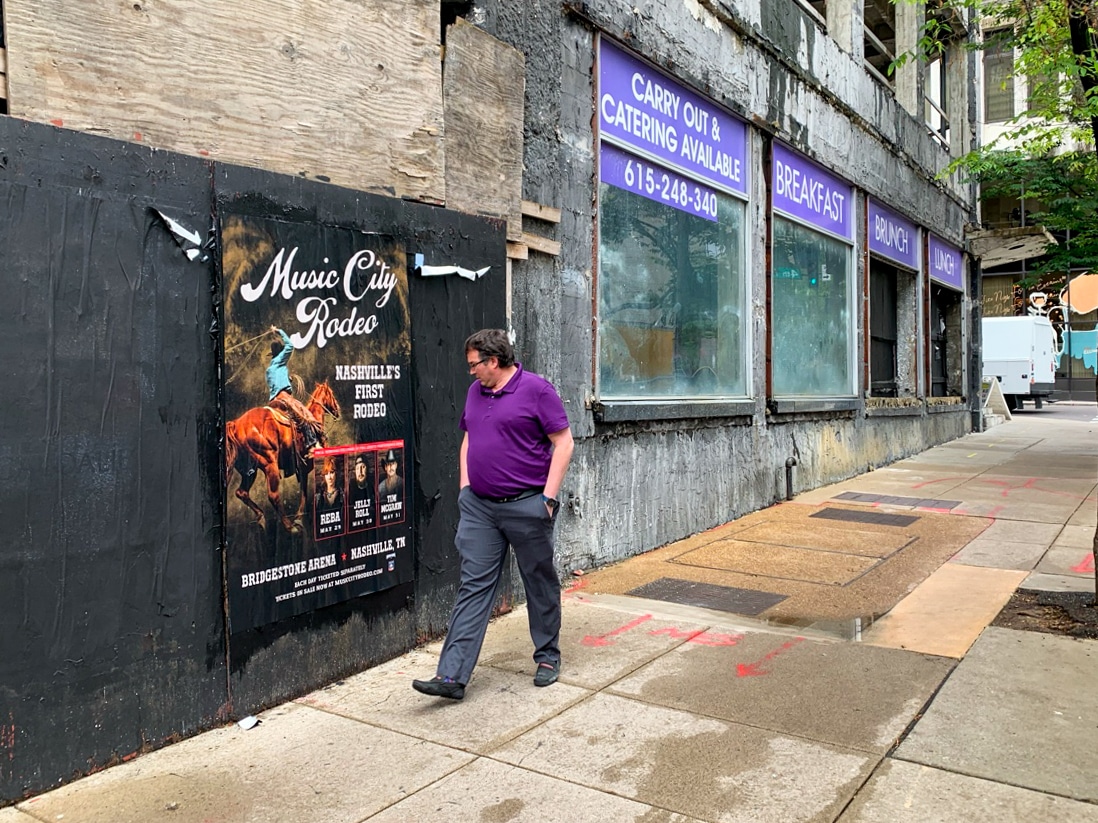 Wild Posting® poster for Music City Rodeo displayed on a boarded storefront wall in Nashville, Tennessee, with a pedestrian walking past.