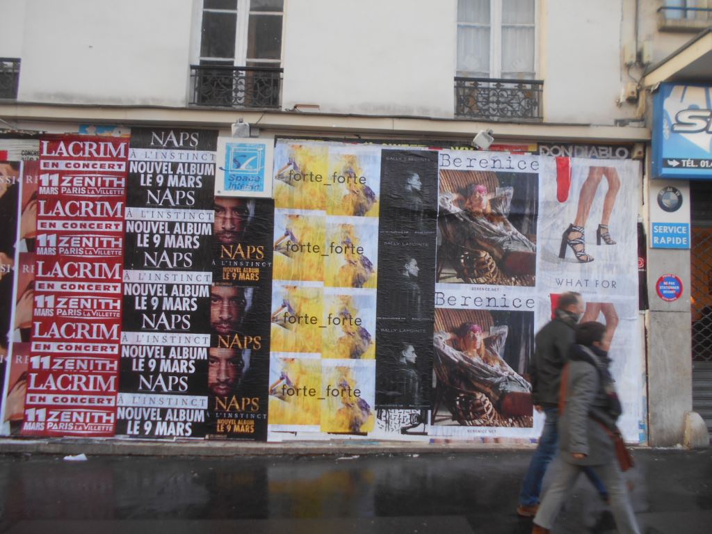 Wild Posting® posters covering a Paris street wall, featuring music and fashion campaigns in a high-foot-traffic area