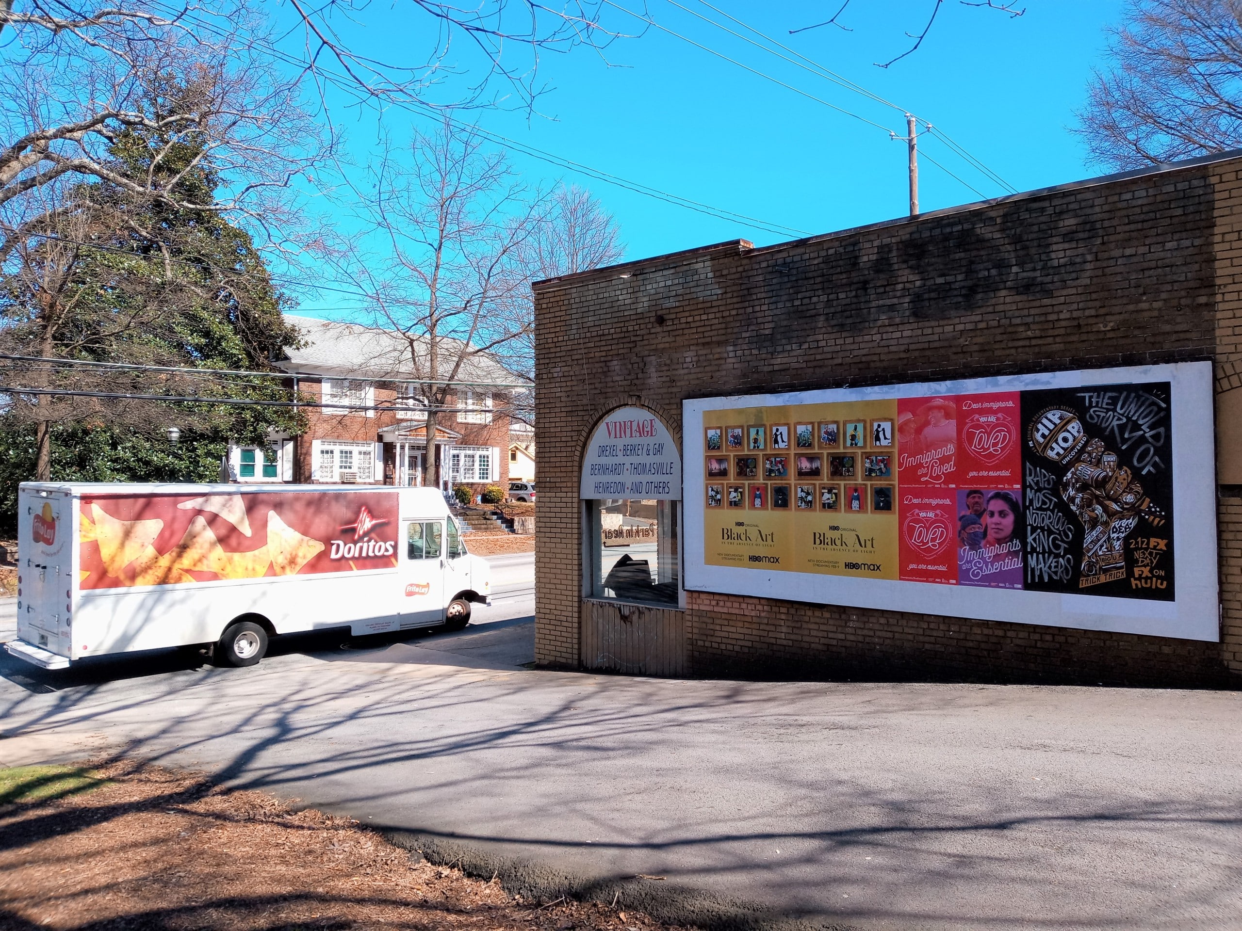 Wild Posting® wall posters for entertainment campaigns on a brick building at Ponce de Leon Ave in Atlanta, with a Doritos-branded truck passing by.