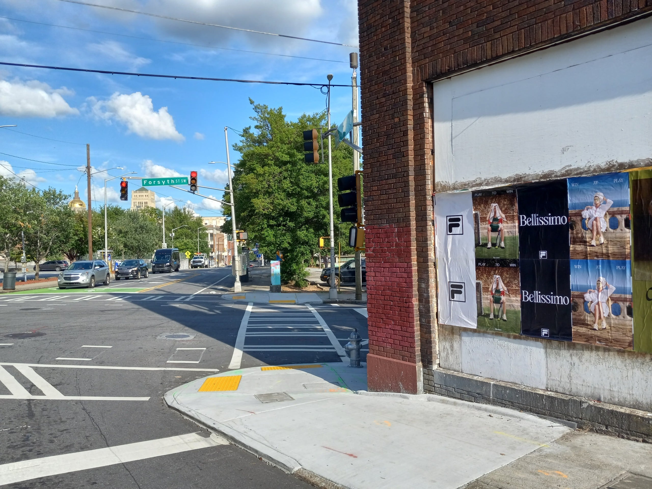 Wild Posting® posters for Fila “Bellissimo” displayed on a brick corner wall at Trinity St & Forsyth St in Atlanta, with a signalized intersection in view.