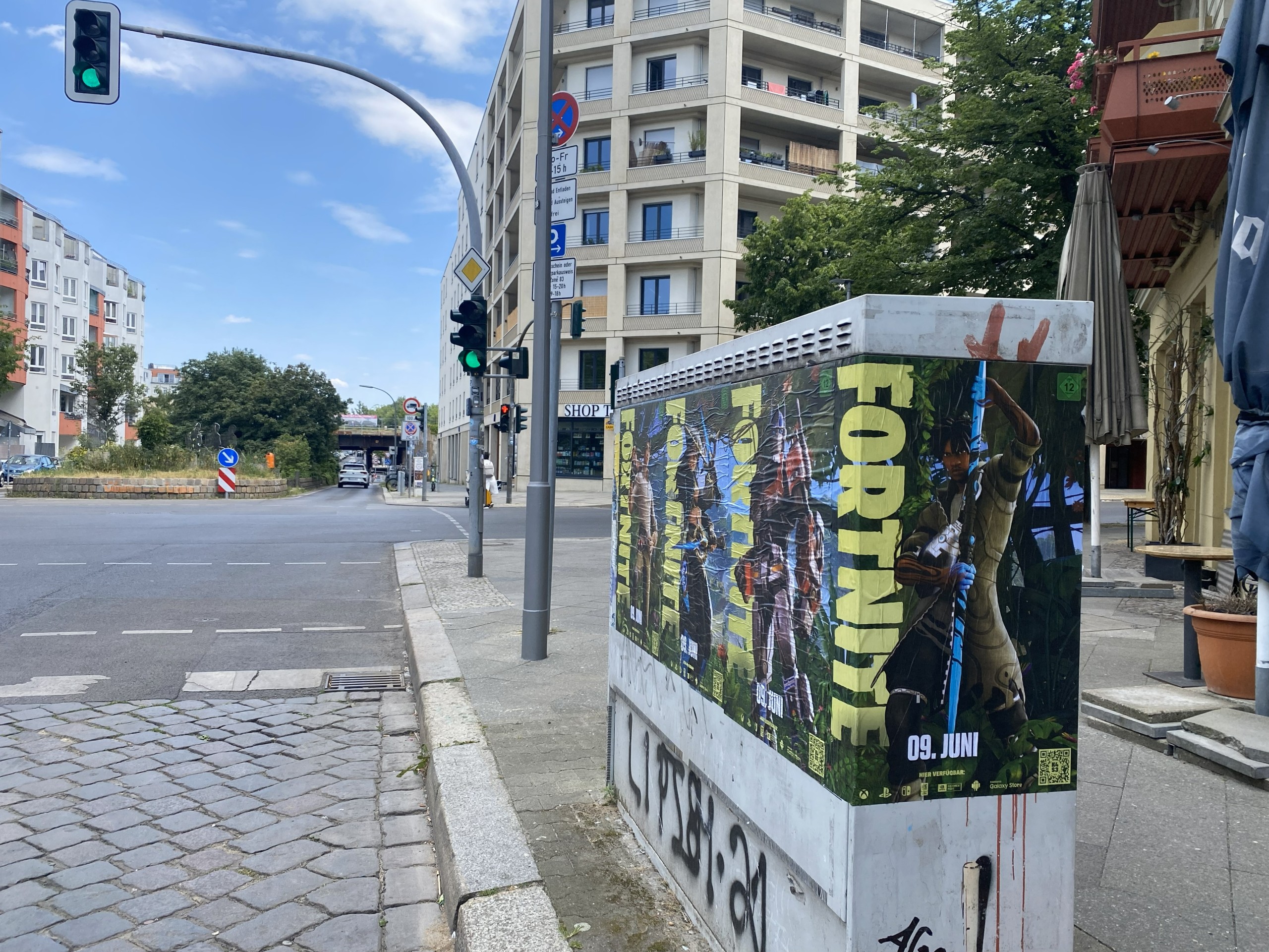 Wild Posting® street posters wrapped around utility box at a busy Berlin intersection with pedestrian and vehicle traffic