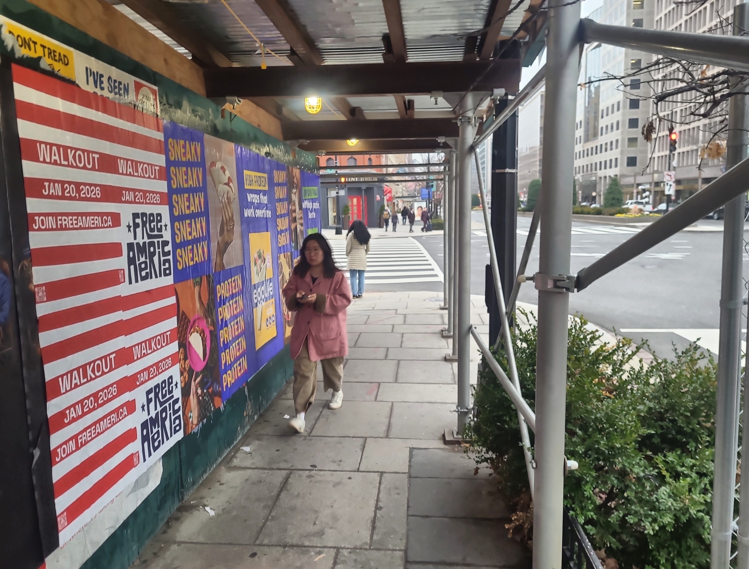 Wild Posting® posters displayed along a scaffolded sidewalk in Washington, DC, with a pedestrian walking past multiple campaign creatives.
